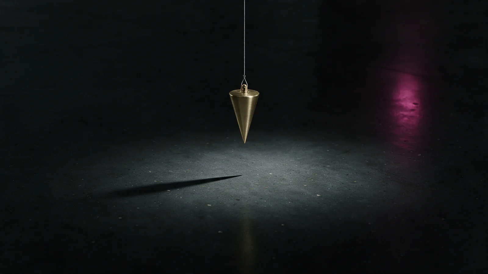 A brass plumb bob suspended on a steel wire above dark polished concrete under a single cold spotlight